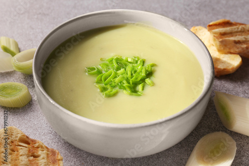 Bowl of delicious soup, cut leek and croutons on grey table, closeup