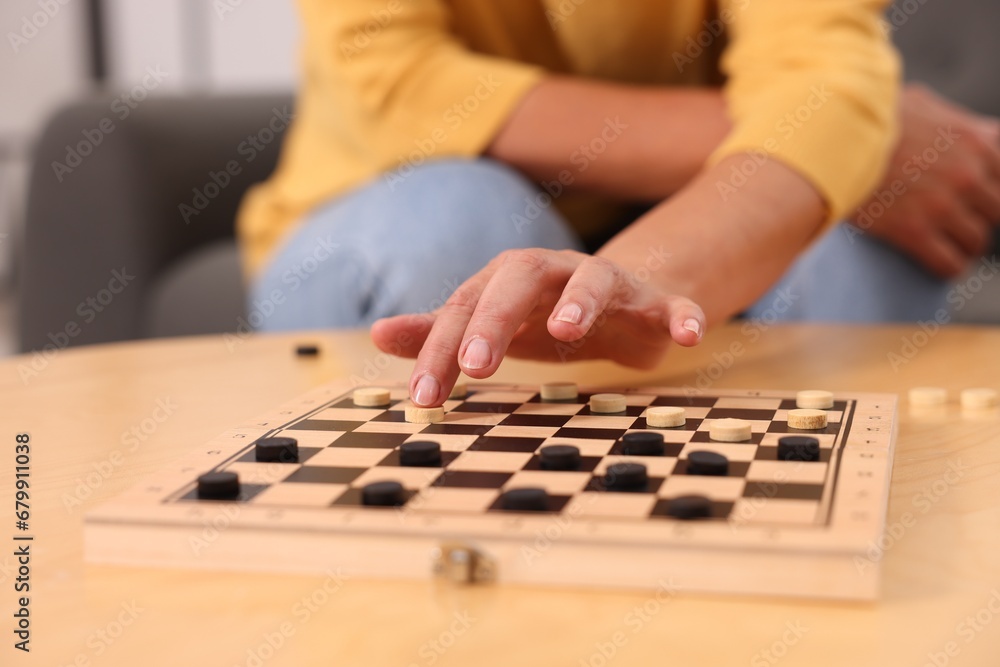 Fototapeta premium Woman playing checkers at wooden table, closeup