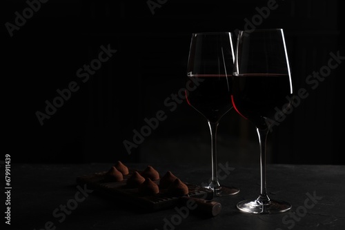 Glasses of red wine and chocolate truffles on black table in darkness, space for text