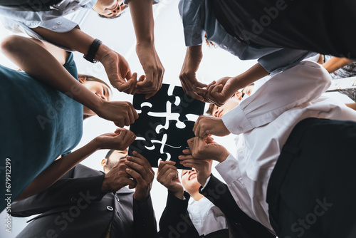 Below view of diverse corporate officer workers collaborate in office connecting puzzle pieces as partnership and teamwork concept. Unity and synergy in business idea by merging jigsaw puzzle. Concord photo