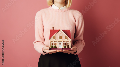 kobieta trzyma w dłoniach makietę domu. 