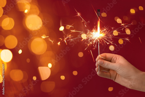 Female hand holding beautiful Christmas sparklers on red background with blurred lights