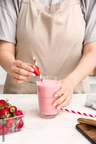 Woman with glass of tasty strawberry smoothie at table in kitchen