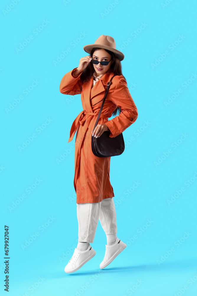 Portrait of fashionable young woman jumping on blue background Portrait of fashionable young woman jumping on blue background