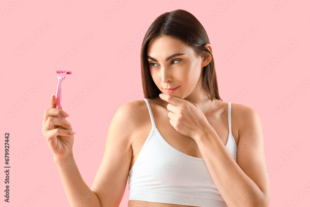 Thoughtful young woman in underwear and with razor on pink background