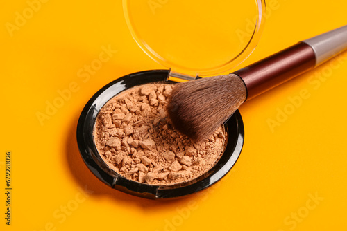 Makeup brush and facial powder on orange background