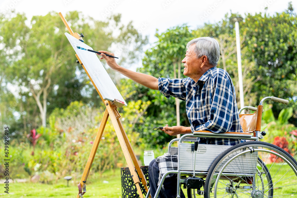 Side view of one Asian senior man sit on wheelchair and paint the painting outdoor for relax and revive good health of old people outside. Side view of one Asian senior man sit on wheelchair and paint the painting outdoor for relax and revive good health of old people outside.
