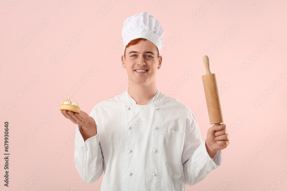 Male confectioner in uniform with lemon tartlet and rolling pin on pink background Male confectioner in uniform with lemon tartlet and rolling pin on pink background