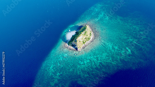 Top view of a small uninhabited island surrounded by a coral reef in the open sea. Aerial view of a rocky uninhabited island with a small sandy beach in the middle of the ocean. © Houston