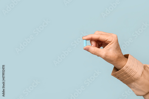 Female hand with pill on blue background