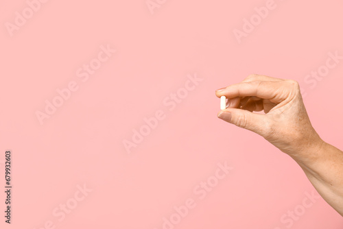 Female hand with pill on pink background