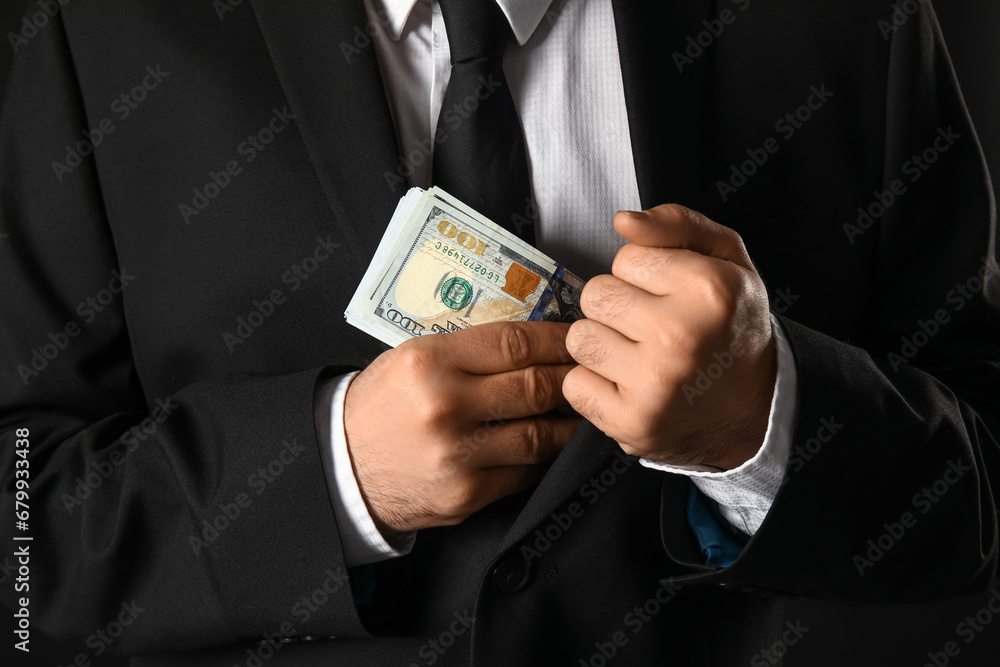 Young businessman putting bribe in jacket on dark background, closeup Young businessman putting bribe in jacket on dark background, closeup