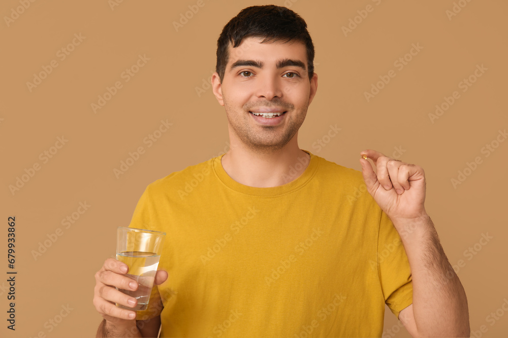 Young man with glass of water and vitamin A pill on beige background Young man with glass of water and vitamin A pill on beige background