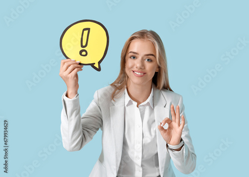 Wallpaper Mural Young businesswoman holding speech bubble with exclamation mark and showing OK gesture on blue background. Business idea concept Torontodigital.ca