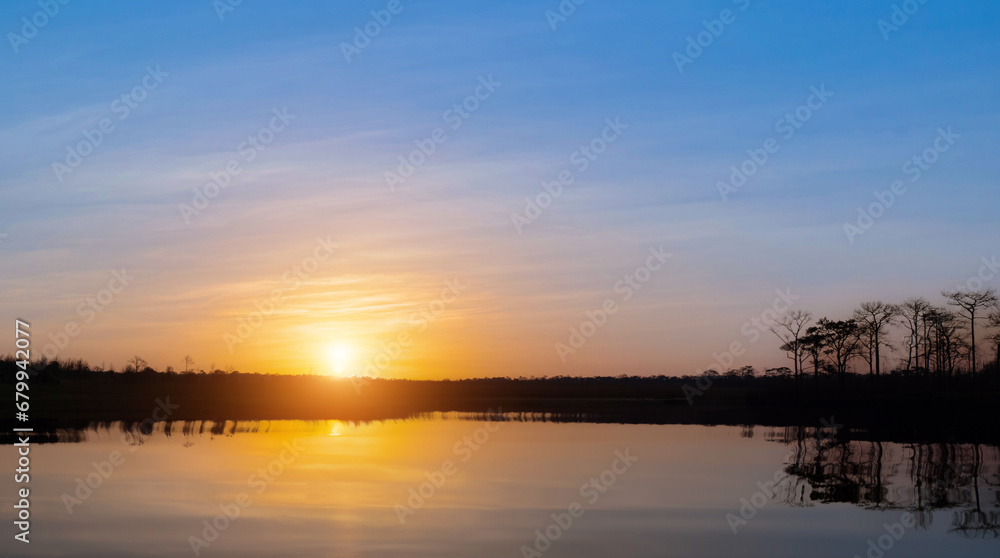 Sunrise at coast of the lake. Blue sky and sun reflection on water. Nature landscape background.
