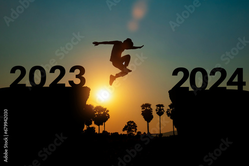 Happy new year 2024 concept. Silhouette of man jump on the cliff between 2023 to 2024 years over sunset or sunrise background. © banphote