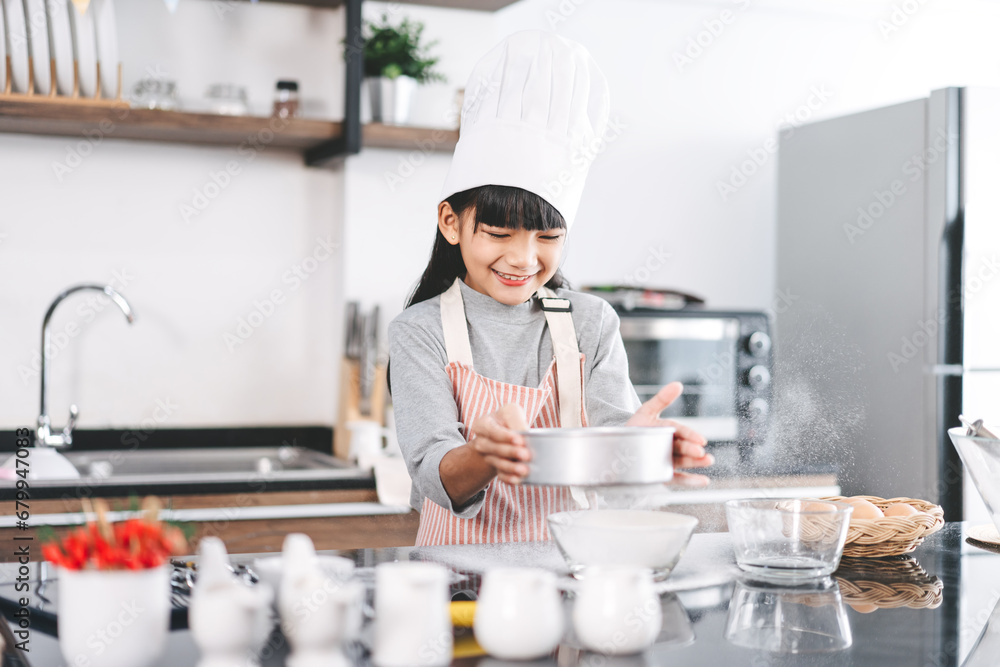 Little asian girl with chef hat and apron cooking in kitchen for homemade bake cake at home Little asian girl with chef hat and apron cooking in kitchen for homemade bake cake at home