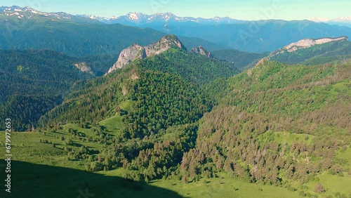 View from the edge of the cliff to the mountains. Panorama from bottom to top. Huge height. Below mountains covered with grass and forest, above mountains in snow. In sky clouds. Hiking in mountains photo