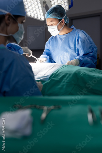 Diverse female doctor with face mask doing surgery in group of doctors in hospital operating room