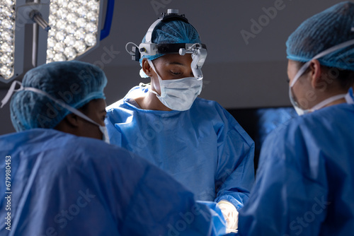 Diverse female doctors with face masks doing surgery in hospital operating room
