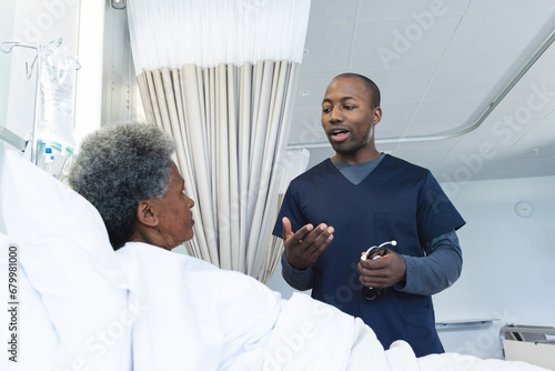 African american male doctor talking with senior female patient in hospital room