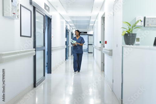 African american female doctor with documents walking in hospital corridor