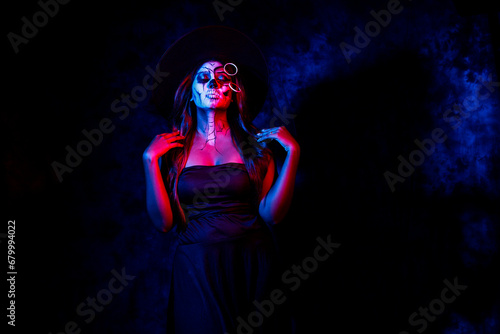 A women with Halloween Makeup in blue red light giving out a horror look wearing black gown in black background © Kaushik