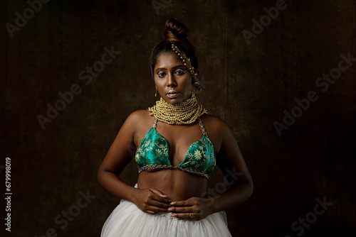 tribal look of a woman wearing blue and white skirt with a bun posing in front of a brown background with gody makeup and beads garland  photo