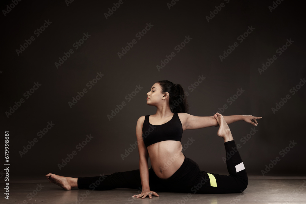 Slim girl performing yoga arts wearing black sports dress in black background performing yoga poses with a flexible body 