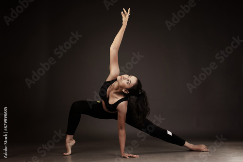 Slim girl performing yoga arts wearing black sports dress in black background performing yoga poses with a flexible body 