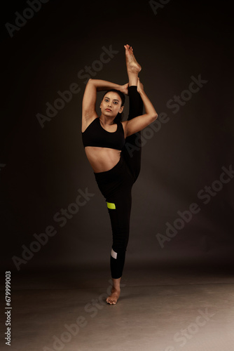 Slim girl performing yoga arts wearing black sports dress in black background performing yoga poses with a flexible body  © Kaushik
