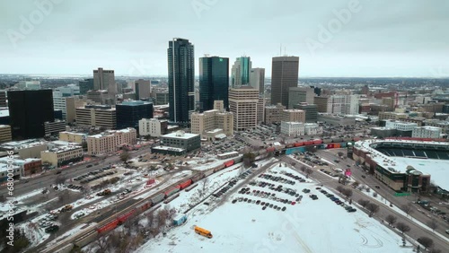 Winnipeg Manitoba Canada Downtown Skyscraper Buildings in City Overcast Landscape Skyline Snowing Winter Drone 4k Drone Shot with Multicolored Train Canadian Museum for Human Rights and Baseball Arena photo