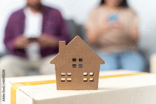 A young couple uses a smartphone to find information about moving house. Male and female and house model.