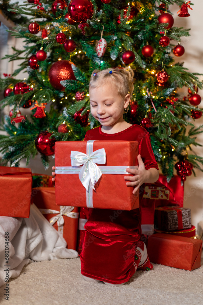 Cute girl with a gift in her hands sits near the Christmas tree. Cute girl with a gift in her hands sits near the Christmas tree.