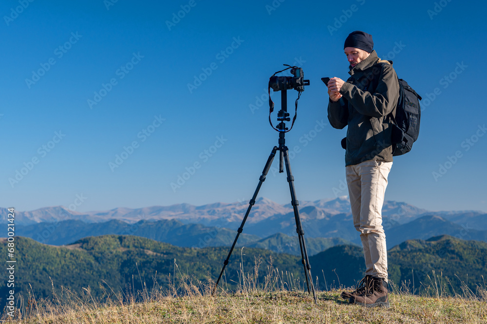 A photographer takes a photo of a beautiful mountain landscape with colorful trees and snow peaks on a sunny autumn day. Traveling through the mountains of Georgia.