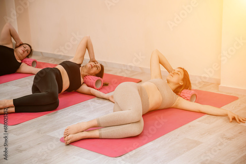 Athletic women doing fascia exercises on the floor with a foam roller massage tool to relieve back tension and relieve muscle pain. The concept of physiotherapy and stretching training