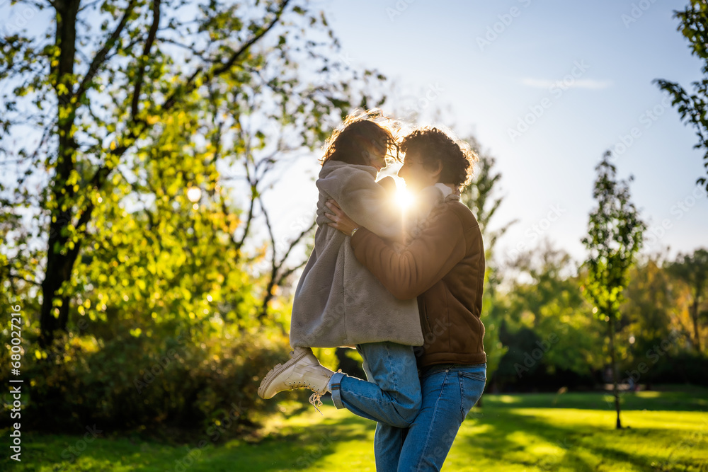 Portrait of happy loving couple in park in sunset. Man is holding his woman in hands.