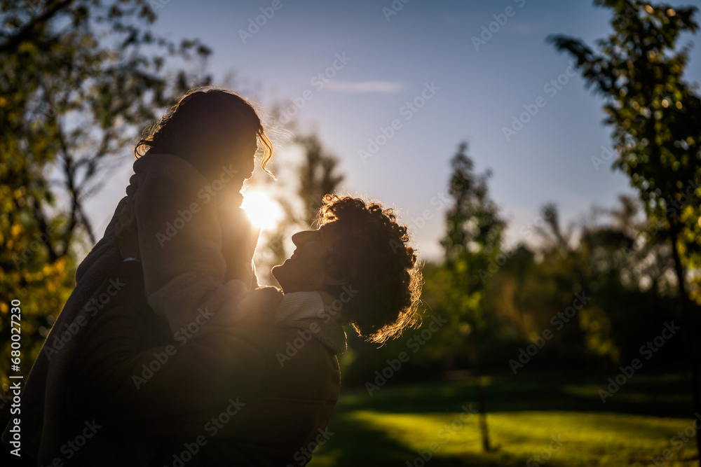 Portrait of happy loving couple in park in sunset. Man is holding his woman in hands.