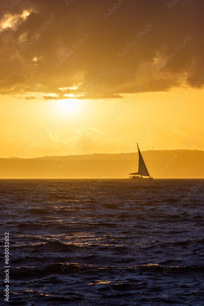 Sailing boat in rought sea at vibrant orange sunset