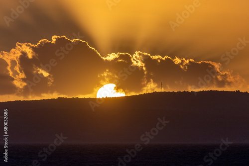 Beautiful sunset on the sea with the sun goes behind the dark silhouette of mountains