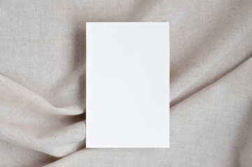 Blank white paper card mockup on neutral beige oat color crumpled linen fabric background with soft shadows, elegant boho wedding invitation or business branding template