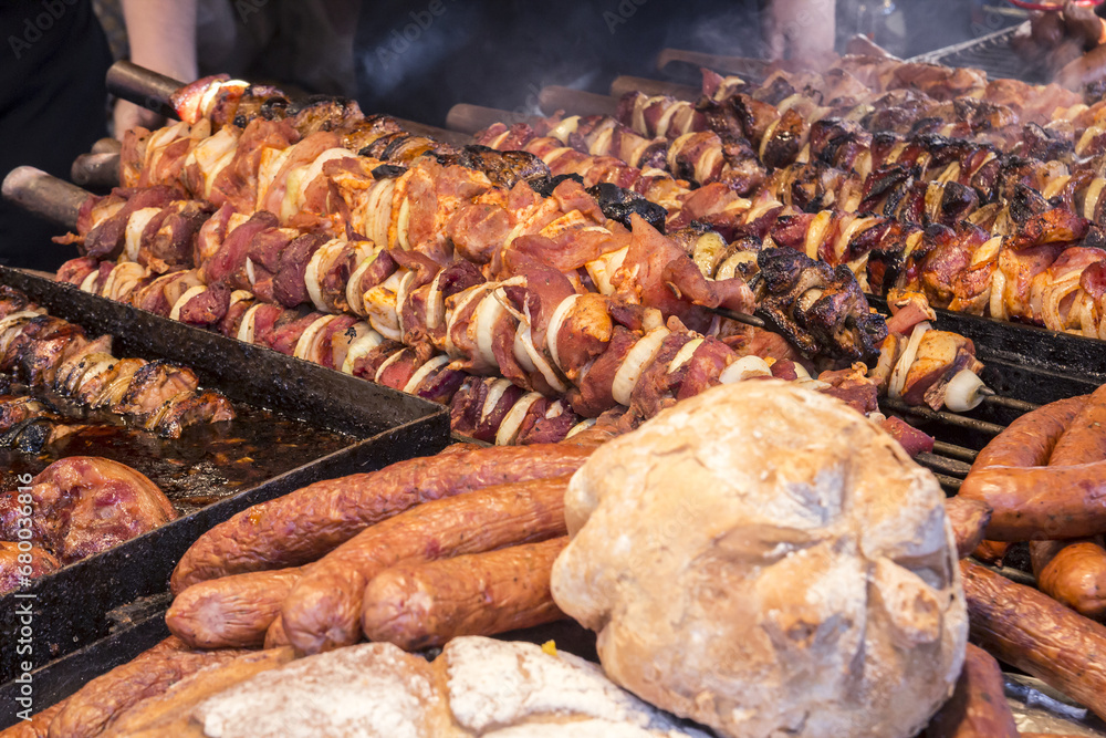 A lot of different meats and sausages are on the counter and grilled,  during the street festival