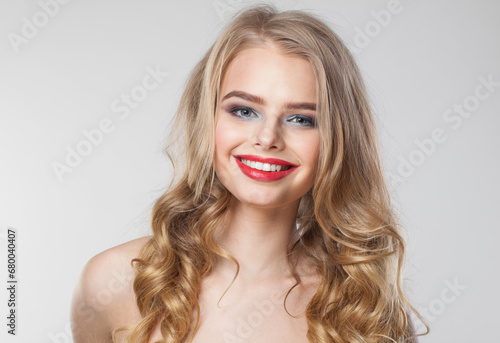 Friendly positive happy woman with makeup and long healthy blonde shiny wavy hair posing against white studio wall background. Emotional fashion beauty portrait