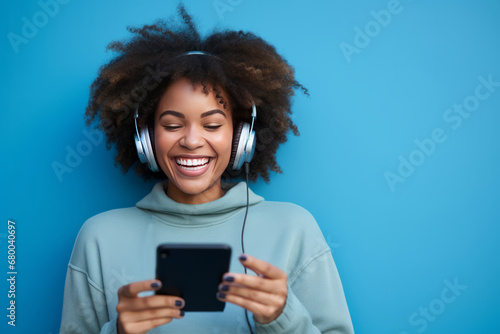 Black woman with afro hair listening to music on a blue background.