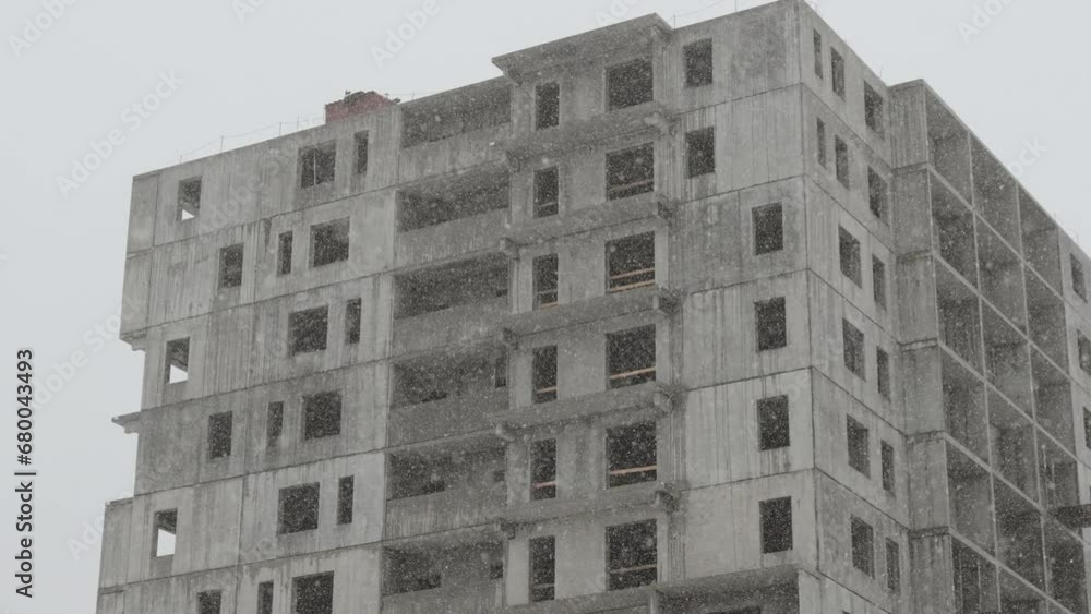 Unfinished wet gloomy building during snowfall in winter. Construction involving loans and mortgages for purchase of apartments. Empty construction site without people and construction stopped. Unfinished wet gloomy building during snowfall in winter. Construction involving loans and mortgages for purchase of apartments. Empty construction site without people and construction stopped.