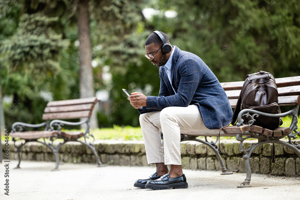 Man in business suit sitting on the bench, listening to the music and relaxing at the park. Man in business suit sitting on the bench, listening to the music and relaxing at the park.