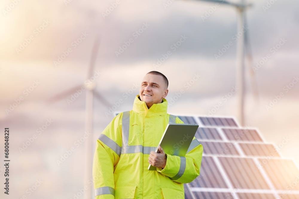 Wind turbine and solar panels engineer. Male engineer maintains and controls wind turbine energy generation on the background of windmills. Concept of sustainable future and green electrical enerygy. - obrazy, fototapety, plakaty 