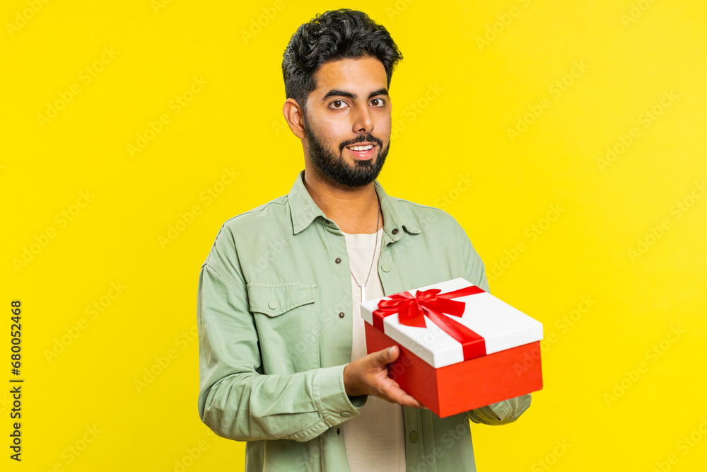 Positive smiling Indian man presenting birthday gift box stretches out hands, offer wrapped present career bonus, celebrating party, promotion discount sale. Arabian guy isolated on yellow background Positive smiling Indian man presenting birthday gift box stretches out hands, offer wrapped present career bonus, celebrating party, promotion discount sale. Arabian guy isolated on yellow background