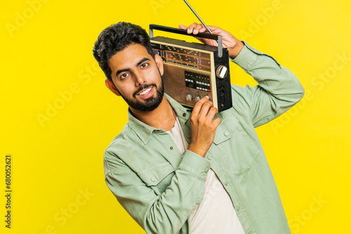 Happy young Indian man using retro tape record player to listen music, disco dancing favorite track, having fun entertaining, fan of vintage technologies. Arabian guy isolated on yellow background