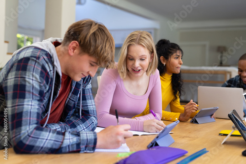 Happy diverse group of teenage friends studying with laptop and tablets at table at home photo